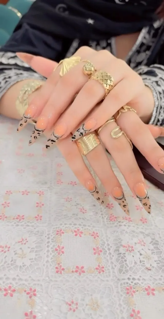 Peach stiletto nails with leopard pattern and gold rings