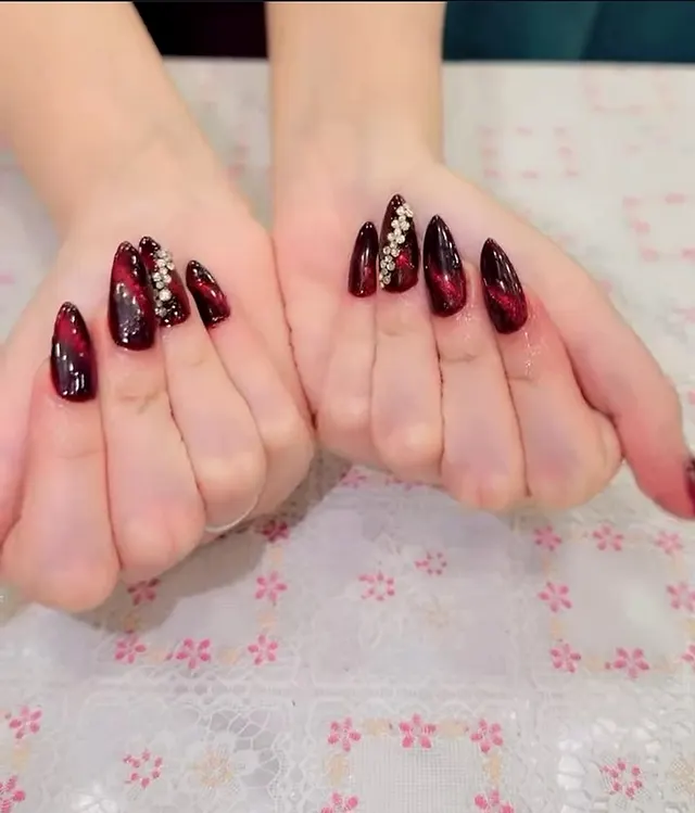 Dark red cat-eye almond nails with rhinestone line